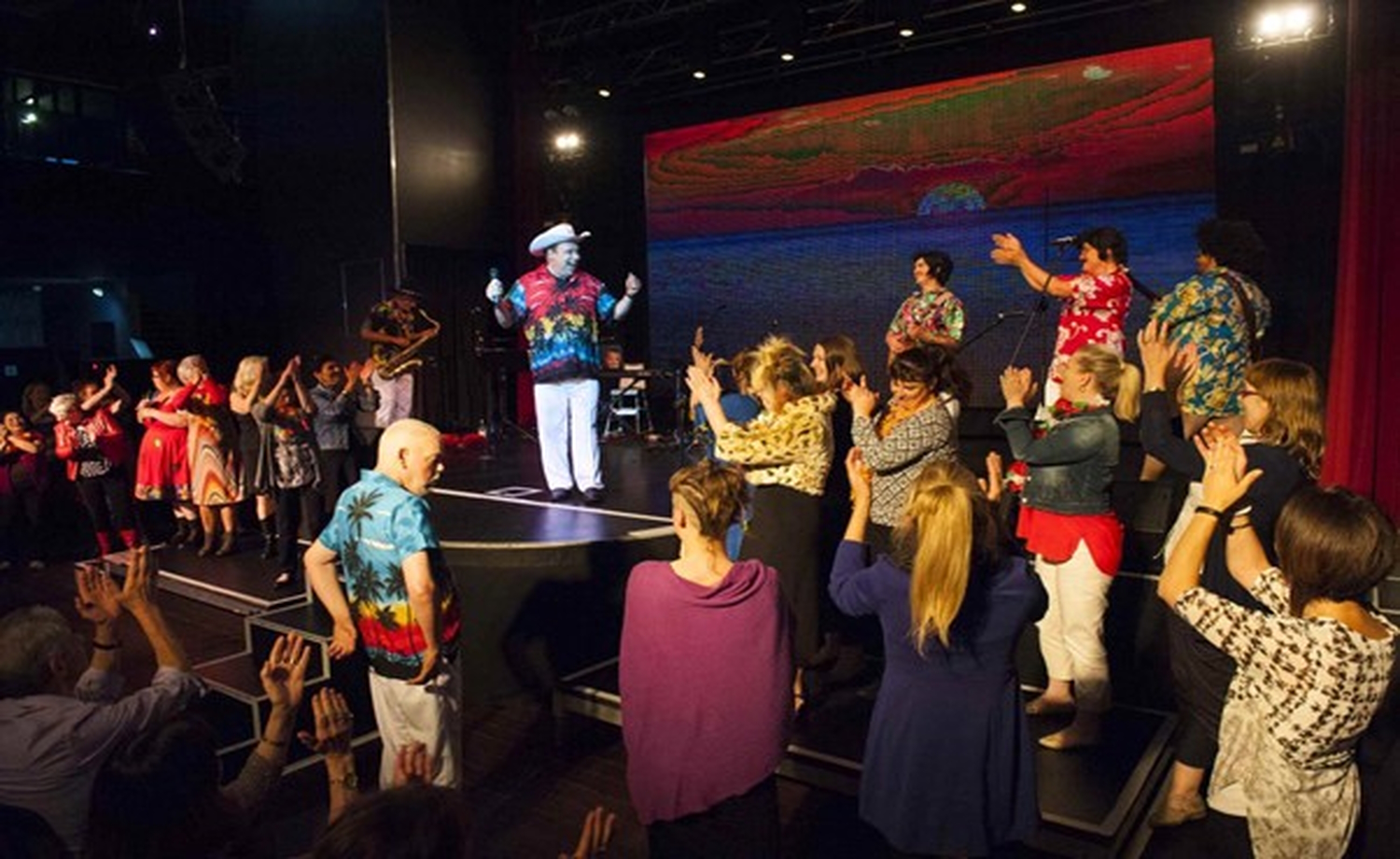 Sparc Theatre's Are You Lonesome Tonight? performance at the Greyhound Hotel. Image of Rodney in cowboy hat and Hawaiian shirt surrounded by a large number of audience members who applaud him energetically. Rodney has both thumbs up, happy in response. Photo by Paul Dunn.